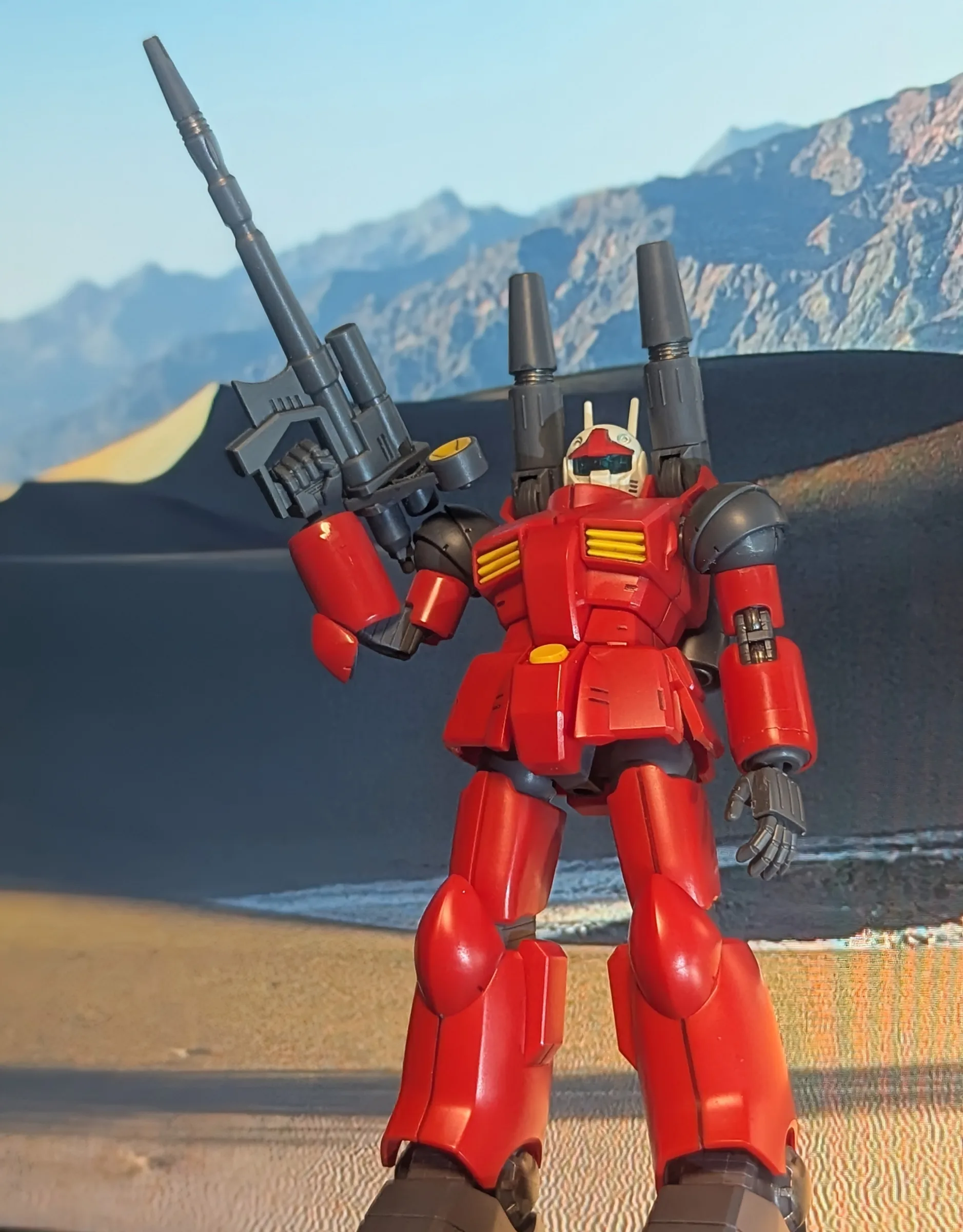 Guncannon holding a rifle in front of desert dunes and mountains